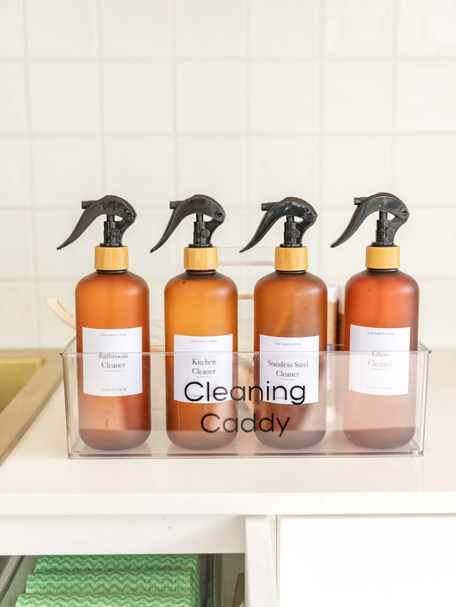 Four spray bottles labeled with cleaning products in a clear container on a kitchen counter.